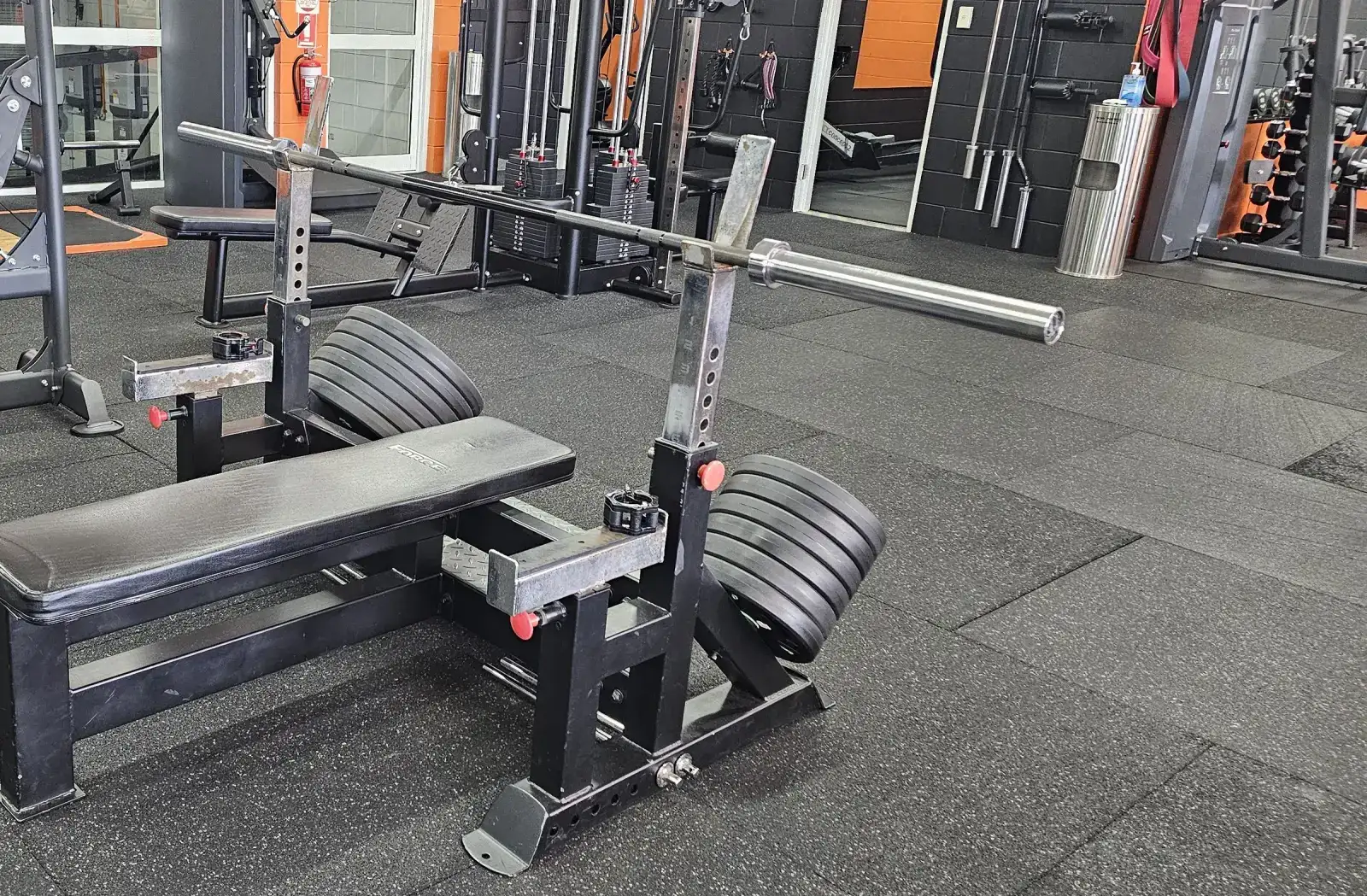 A loaded flat bench press station on the main floor at Get Fit Burdekin, with cable machines and barbells along the wall behind