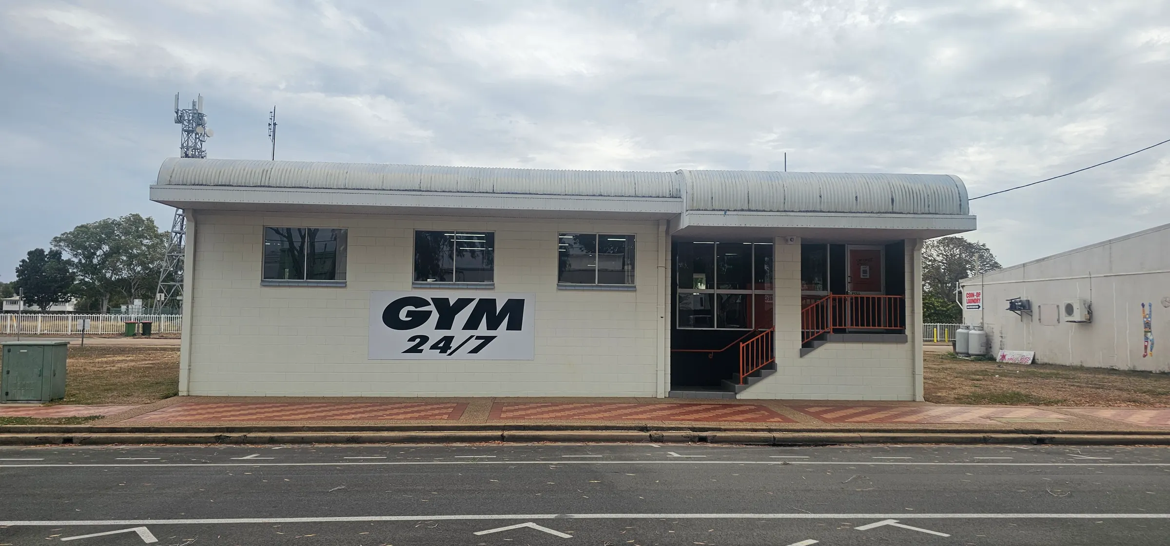 The Get Fit Burdekin building from across Eighth Avenue, Home Hill: a cream block building with a curved roof, a GYM 24/7 sign on the front wall and orange-railed steps up to the entrance