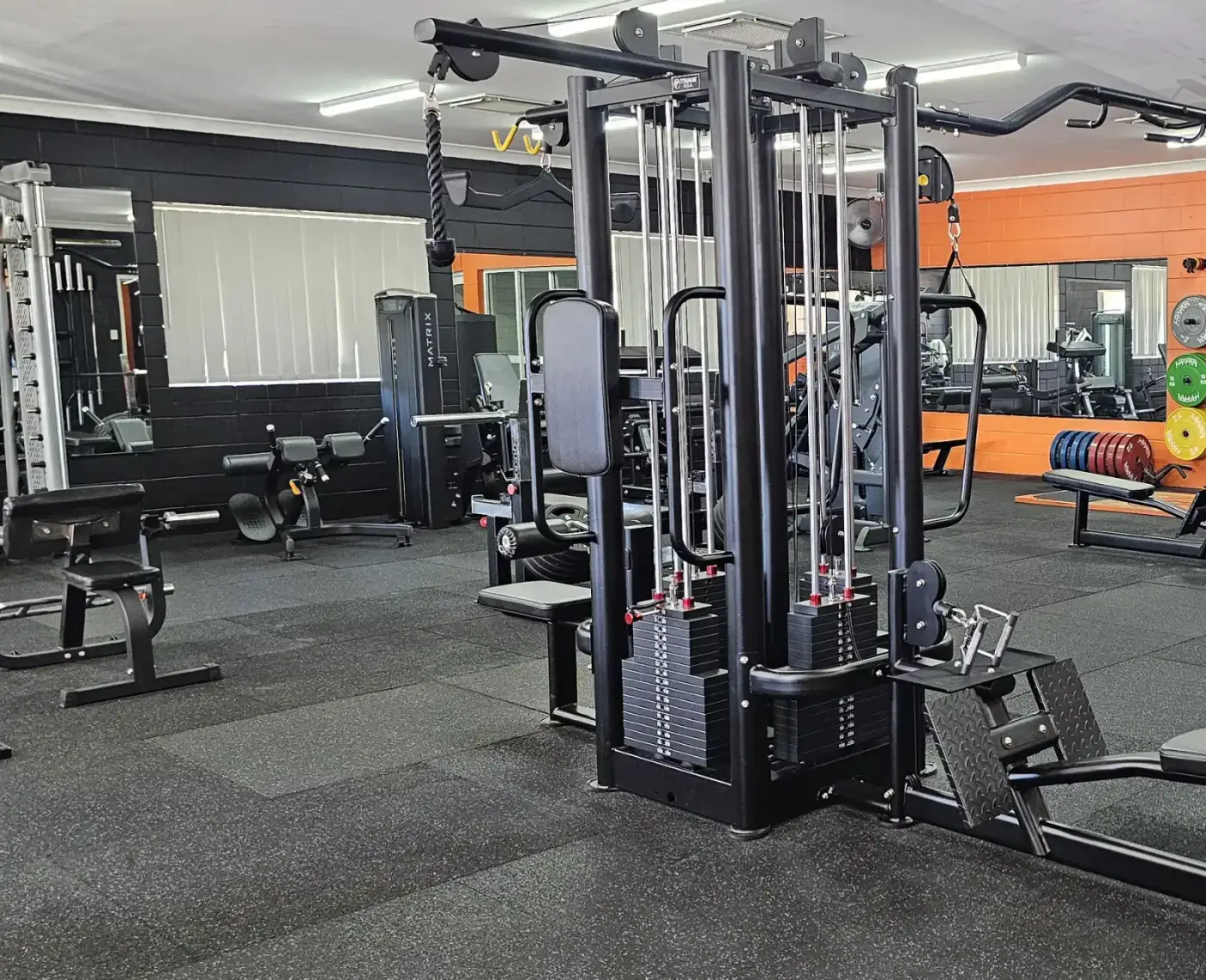 The main floor at Get Fit Burdekin in Home Hill, with a multi-station cable machine, benches and the orange feature wall
