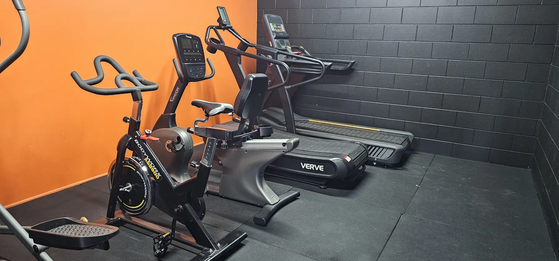 The cardio room at Get Fit Burdekin, with a spin bike, a recumbent bike and two treadmills against the orange and black walls
