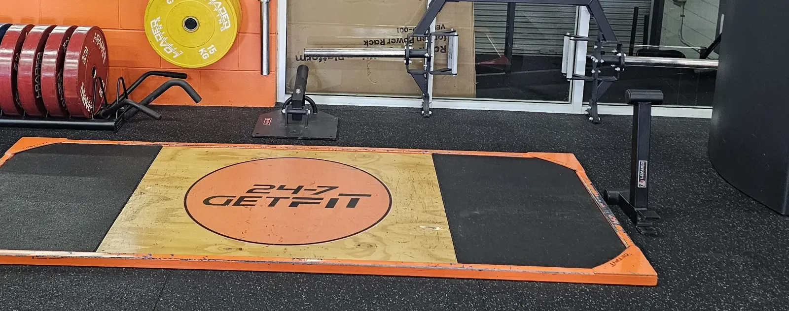 The deadlift platform marked 24/7 Get Fit, with a trap bar and a rack of coloured bumper plates