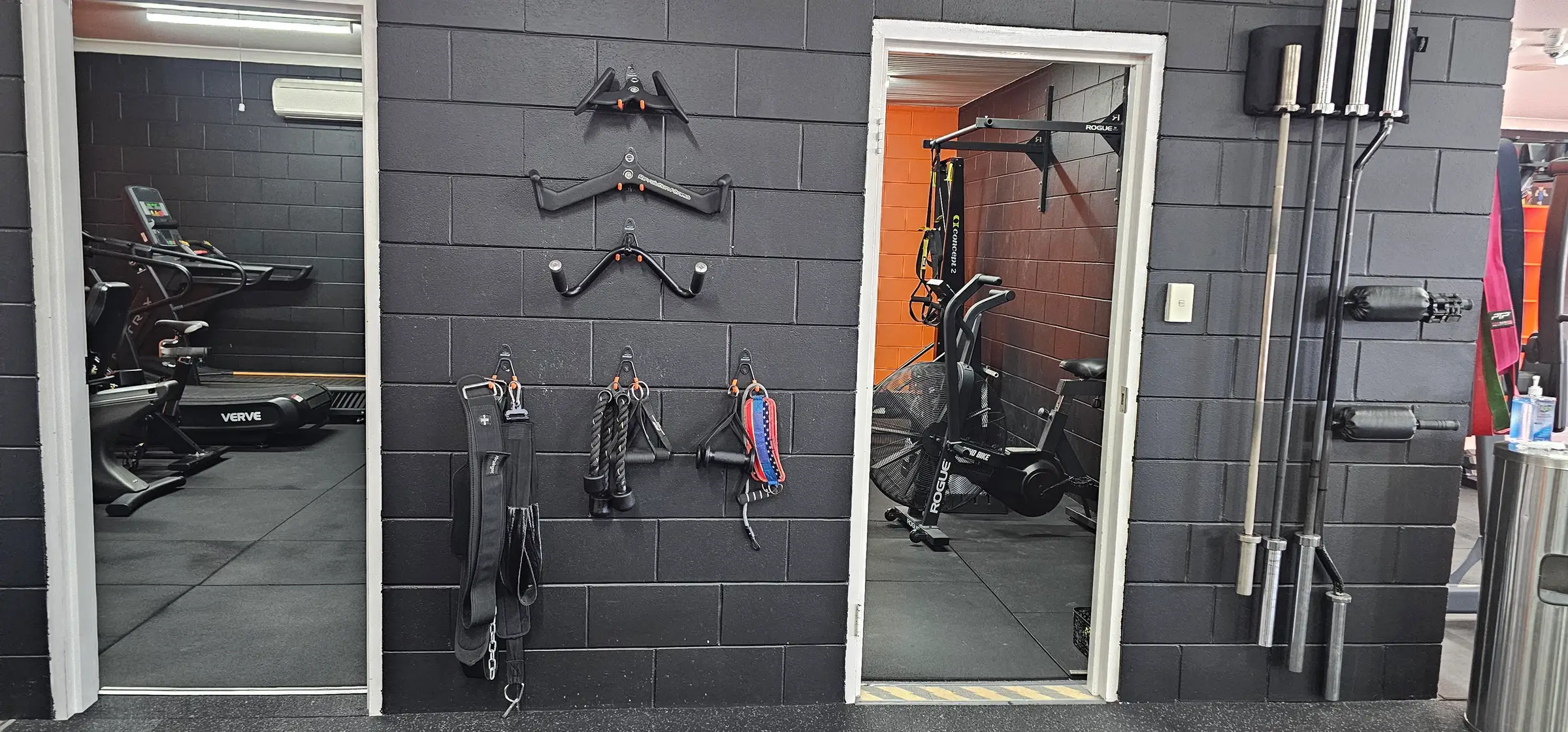 Two doorways off the main floor at Get Fit Burdekin, with cable handles, ropes and straps hung on the black brick wall between them