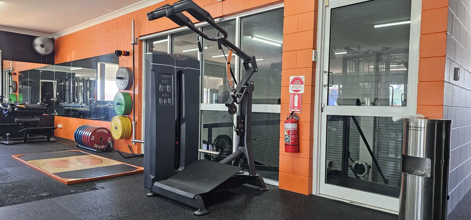 Inside Get Fit Burdekin in Home Hill, with a hack squat machine beside the glass doors and the lifting platform and bumper plates behind