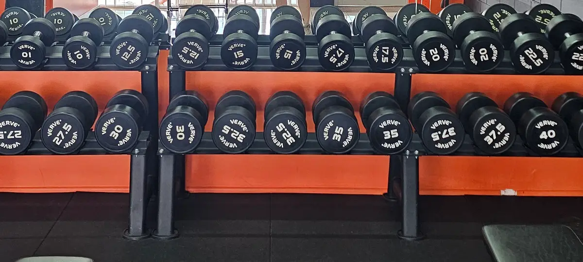 Pairs of rubber dumbbells on two racks against the orange wall at Get Fit Burdekin