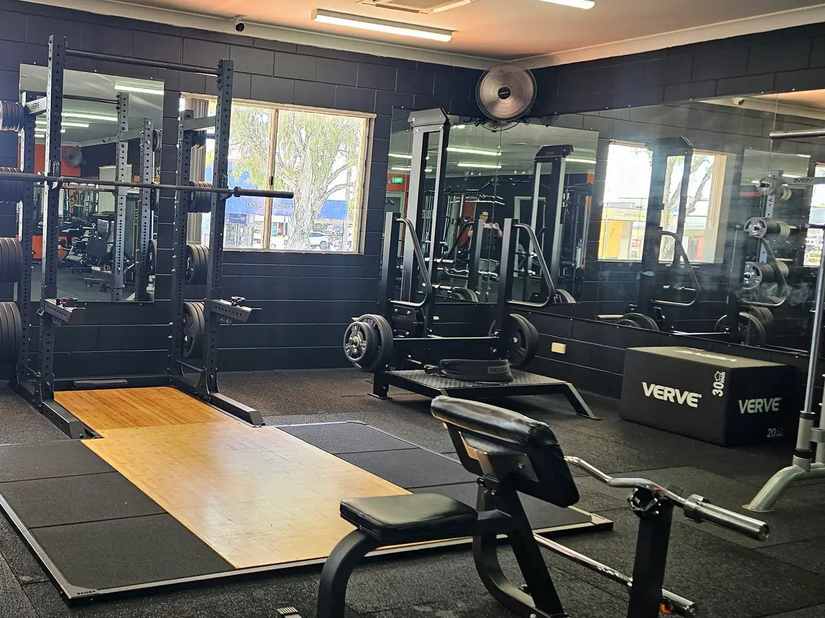 A squat rack over a timber lifting platform under the front windows at Get Fit Burdekin, with a bench and plyo boxes beside it