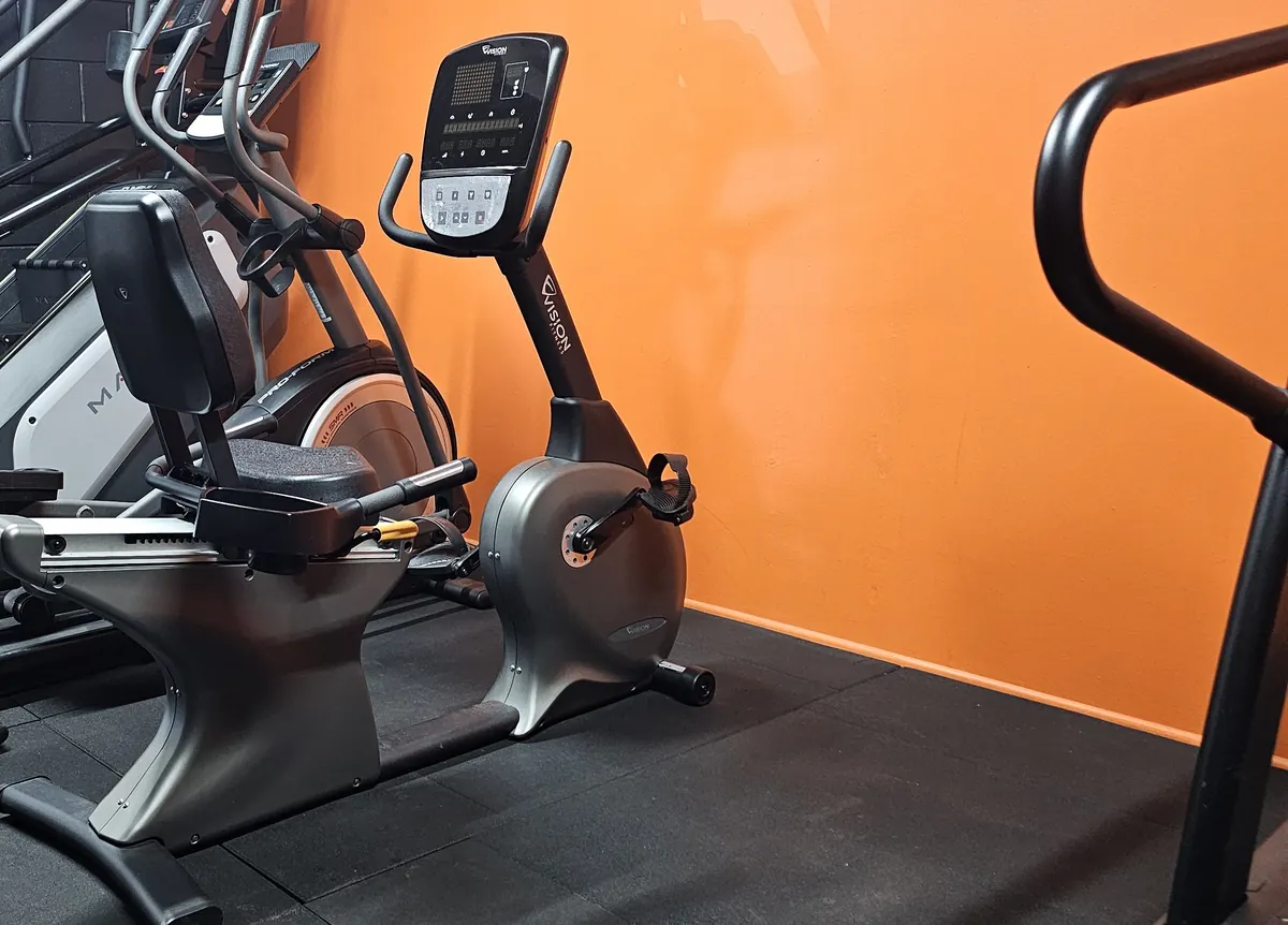 A recumbent exercise bike and an upright bike against the orange wall at Get Fit Burdekin