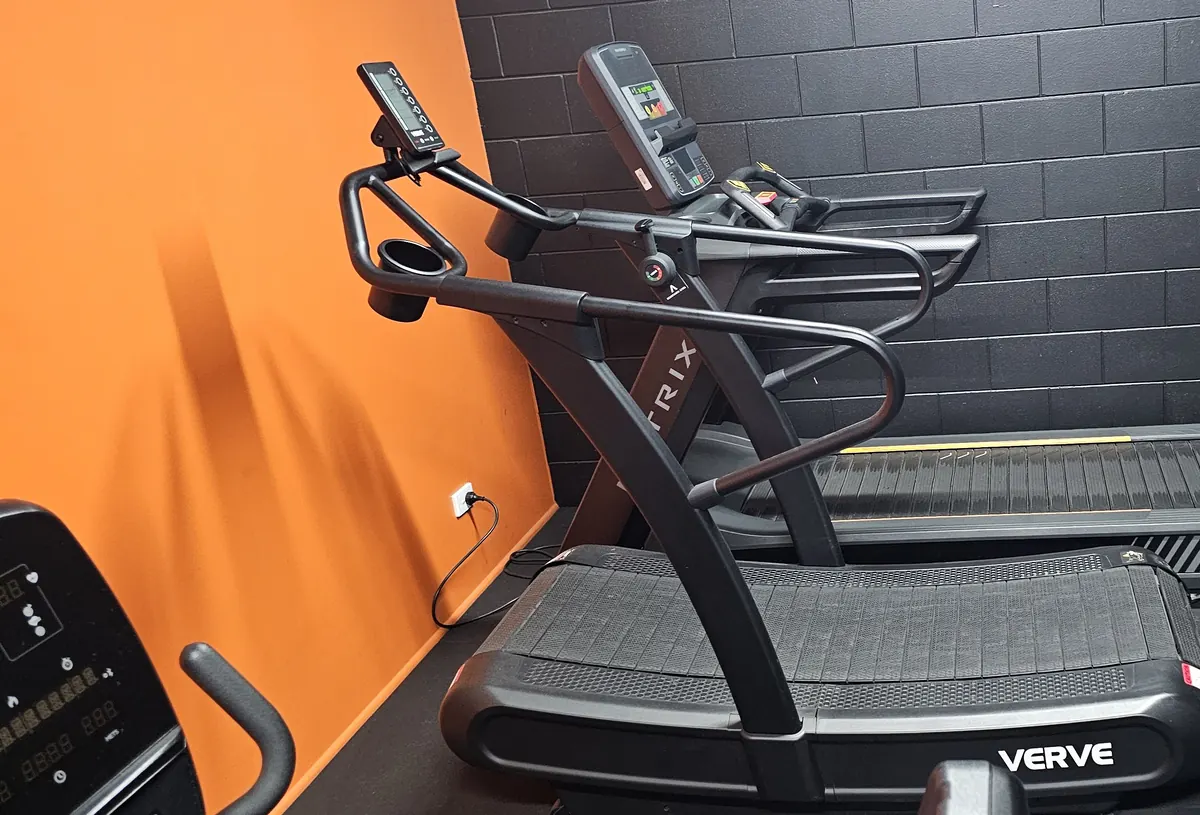 A motorised treadmill beside a Verve curved non-motorised runmill against the orange wall of the cardio room