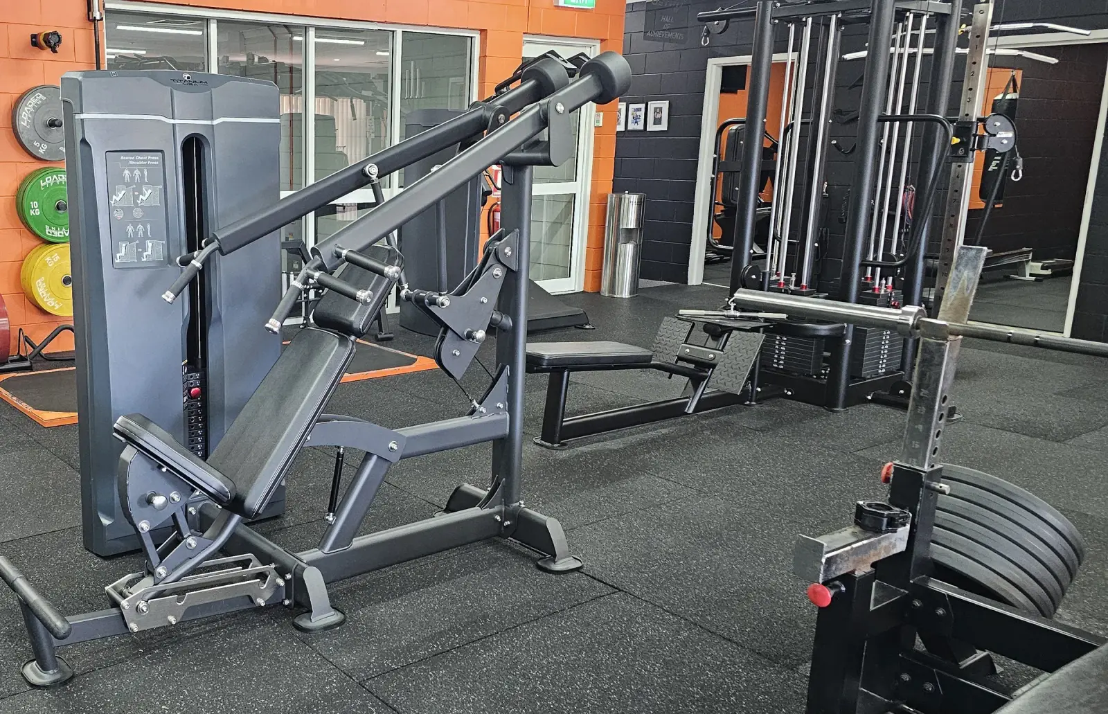 The main floor at Get Fit Burdekin in Home Hill, with a pin-loaded press machine in front of bumper plates and cable machines along the orange wall