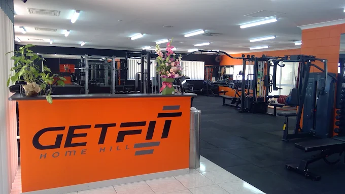The front counter at the gym, with the GET FIT logo on the orange desk and the gym floor behind it